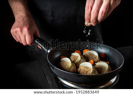 Cooking cutlets on grill pan by chef hands on black background for copy space text restaurant menu. The chef adds salt