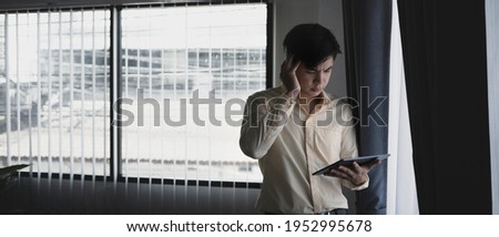 Serious businessman looking at tablet computer and feeling stressed while standing in office.
