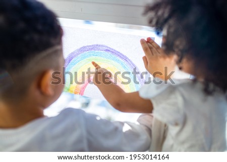 two brazilian ethnic kids with rainbow painted with colorful window color staying at house indoor