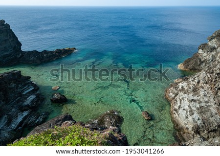 Impressive marine scene seen from a high cliff. Well designed coral platform with large rocks, transparent sea and a deep navy blue in the background.