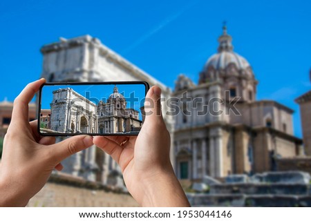 Tourist taking photo of ancient ruins in a summer day in Roman Forum in Rome, Italy. Man holding phone and taking picture arch of Emperor Septimius Severus and church Santi Luca e Martina.