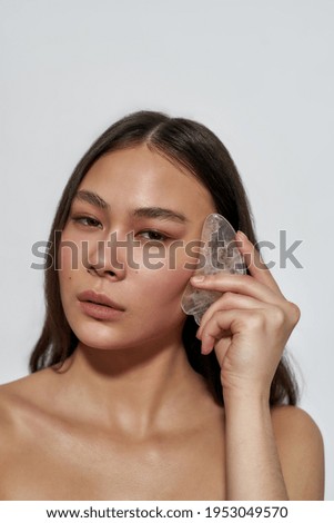 Beautiful asian girl posing in studio with facial massager. Concept of a well-grooming girl in the studio. Brunette with clear skin gives a massage for soft skin