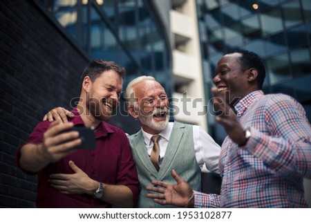 Cheerfully self portrait.  Three business men standing outside and using mobile phone. 