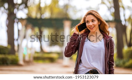 Young natural and smiling girl talks with her smartphone in the park