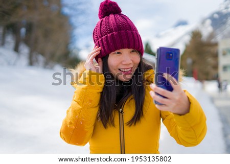 winter holidays in Swiss Alps - young beautiful and happy Asian Korean woman  taking selfie with mobile phone on snow landscape smiling cheerful in the cold mountain