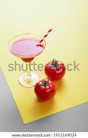Glass with tomato juice and straw and tomatoes.