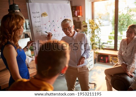 An elderly female boss holds a presentation to her colleagues in a pleasant atmosphere at workplace. Business, office, job