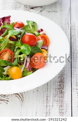 Fresh salad with cherry tomatoes and basil leaves in a plate on white wooden table