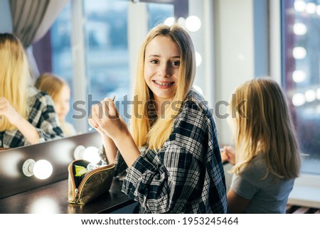 Life of a teenager, a girl with braces on her teeth smiles looking into the camera. Blonde girl in a shirt posing in front of the mirror in the dressing room.