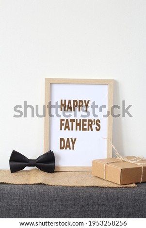 Frame with text "Happy Father's Day", bow tie, and gift on white background.