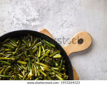 Top view of fried garlic arrows in a black pan.