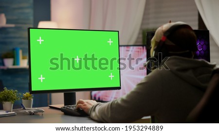 Professional cyber gamer playing video games with greenscreen, chroma key, mock up desktop isolated display. Player using powerful computer with mockup screen streaming shooter games wearing headset