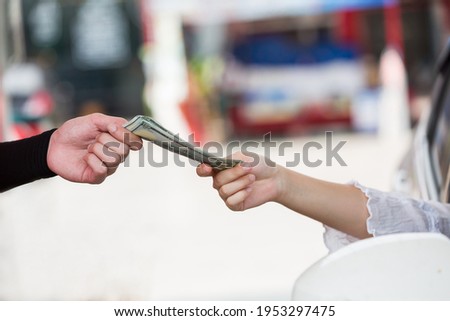 Closeup of hand of service worker receiving money from hand of customer at gas station. Hand of people giving money to hand of worker at oil station. Refuelling car and paying by cash at gas pump