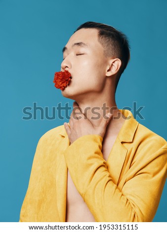 Man with a flower on his teeth yellow jacket blue background portrait asian appearance