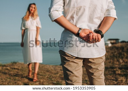 A young man in love is preparing to make his girlfriend an offer to marry, hiding the ring behind his back. A couple in love at the sea, the engagement scene before the wedding. Wedding proposal.