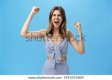Excited and thrilled overwhelmed attractive woman in matching stylish clothes becoming fan of football standing on stadium yelling to cheer team raising clenched fists in rage and victory gesture