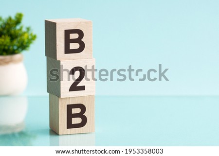 Three wooden cubes with letters - b2b - short for business to business, on blue table, space for text in right. Front view concepts, flower in the background.