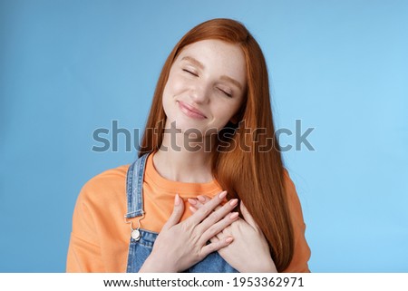 Dreamy touched romantic ginger girlfriend close eyes recalling heartwarming romance touch heart palms pressed chest smiling tenderly feel love care sympathy express affection, blue background Royalty-Free Stock Photo #1953362971