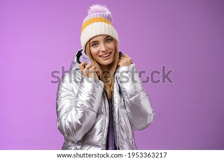Tender feminine gentle blond girlfriend posing boyfriend take pictures ski resort holiday wearing glittering stylish jacket winter hat standing pleased purple background smiling delighted