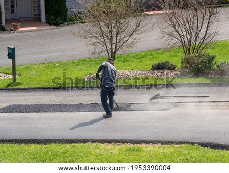 Worker applying a layer of tarmac or extra blacktop to repair damage to asphalt street Royalty-Free Stock Photo #1953390004