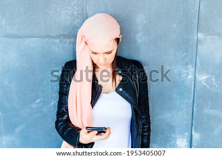 Woman with cancer and pink headscarf checking results on mobile phone with tired face and very serious . fight against cancer concept
