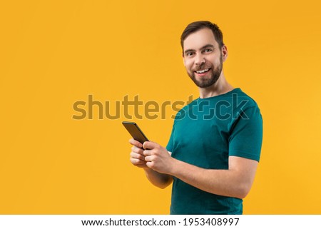 Attractive smiling bearded man with smartphone in hands looking happy winning money after betting online at bookmaker's website using mobile application. Copy space for your text or logo.  Royalty-Free Stock Photo #1953408997