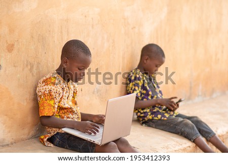 one african kid using a laptop and the other using a mobile phone Royalty-Free Stock Photo #1953412393