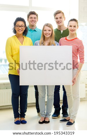 education, advertising and school concept - five smiling students with white blank board at school