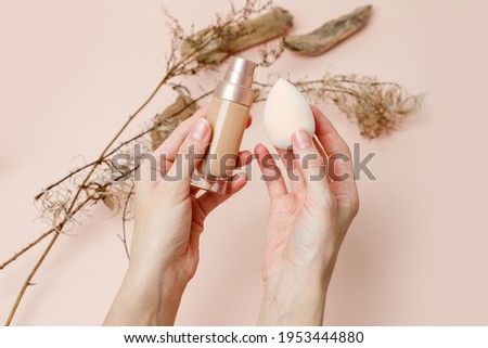 Foundation with make up beuty blender in female hands on a trendy beige brown earth tones background. BB cream for professional make-up. Cosmetic female accessory, liquid fluid, stylish Royalty-Free Stock Photo #1953444880