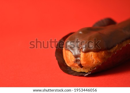 Macro photographie shot of classic French chocolate dessert eclair filled with custard isolated on red background. Copy space image