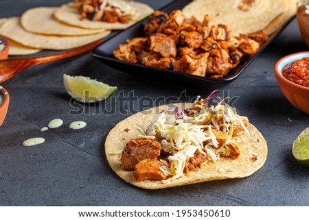 Closeup image of a Mexican taco dish with corn tortillas, precooked, preseasoned chicken pieces, cabbage slaw, shredded cheese, salsa and cream sauce and lime slices. Angled selective focus image.