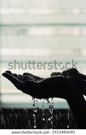 Silhouette of a man's hand under a shower against a backlit window.