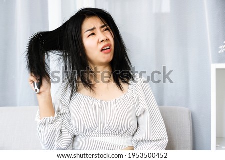 upset Asian woman using comp brushing her dry ,damaged hair unhappy with messy hair  Royalty-Free Stock Photo #1953500452