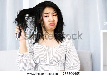 upset Asian woman using comp brushing her dry ,damaged hair unhappy with messy hair  Royalty-Free Stock Photo #1953500455