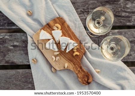 Two glasses of white wine and a wooden plate with cheese and nuts served outside at sunset. Royalty-Free Stock Photo #1953570400