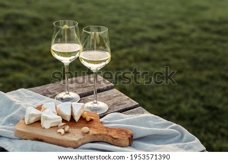 Two glasses of white wine and a wooden plate with cheese and nuts served outside at sunset. Royalty-Free Stock Photo #1953571390