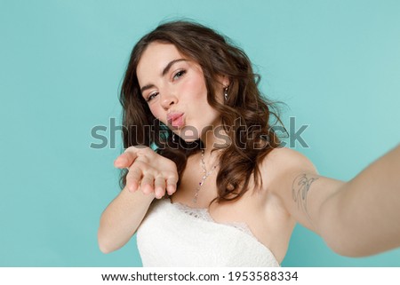 Close up of pretty bride young woman in white wedding dress doing selfie shot on mobile phone blowing sending air kiss isolated on blue turquoise background studio. Ceremony celebration party concept
