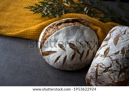 Two freshly baked sourdough breads on a table. Top view photo of round bread  made of whole grain, yellow linen towel. Grey textured background. 