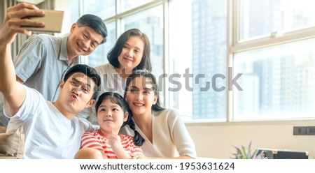 asian multi generation family parent and grand parent with little daughter child sit relax on sofa in living room take selfie with smartphone together with smiling and cheerful laugh smile at home