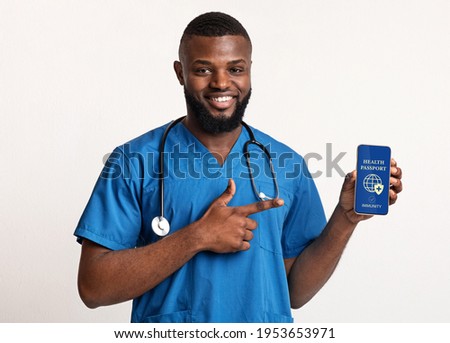 Healthcare And Medicine. Young African American male doctor holding cellphone with digital international health passport, pointing at screen, showing proof that he has immunity for coronavirus disease