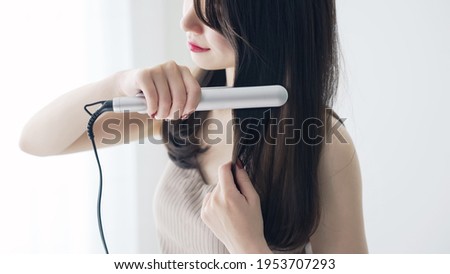 Young asian woman using a curling iron. Hair care concept. Royalty-Free Stock Photo #1953707293