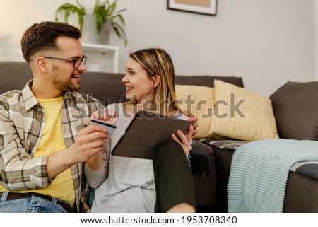 Online shopping. Photo of smiling couple shopping online, man holding a credit card while woman holding tablet computer and doing a payment.