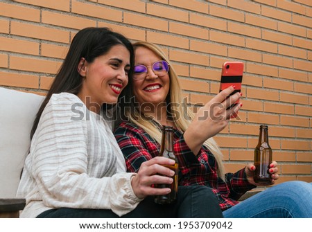 Two smiling young friends drinking beers and taking selfies with a mobile on a terrace