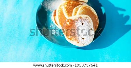 A bunch of hole pancakes with powdered sugar on a turquoise ceramic plate. Copy space on a turquoise background.