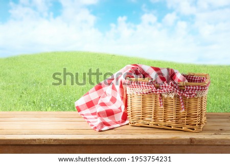 Empty picnic basket and tablecloth on wooden table over landscape background. Shavuot holiday mock up for design. Royalty-Free Stock Photo #1953754231