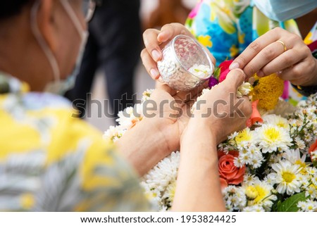 Hand holding silver bowl to pouring scented water on the hands of revered senior people and ask for blessing and greeting in songkran day with COVID-19 is thought to spread. Thailand new year. Royalty-Free Stock Photo #1953824425