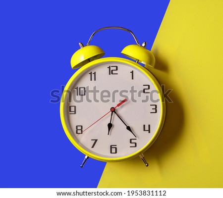 Illuminating color Retro style alarm clock on blue and yellow background, top view.