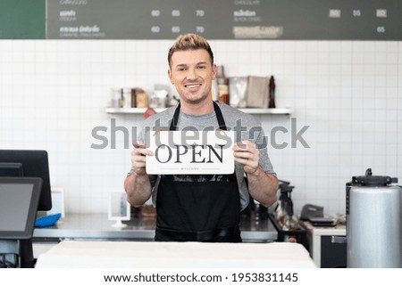 Barista cafe wear apron holding open sign at coffee shop with happy and smile. Small business owner and startup raising opening sign for service customer