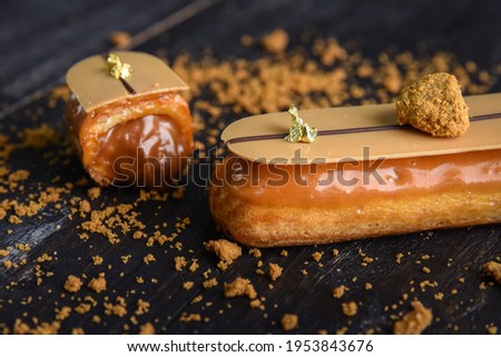 Glazed eclair with caramel filling, decorated with a chocolate bar with edible gold. Eclair in a cut with a flowing filling. Royalty-Free Stock Photo #1953843676