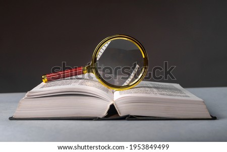 Open book closeup with turning pages and magnifying loupe. Textbook in hard cover on table. Studying and research concept. Royalty-Free Stock Photo #1953849499
